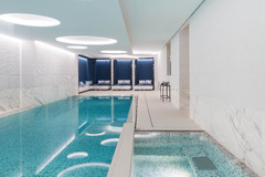 Indoor swimming pool with sleek modern design, white marble walls, and lounge chairs at The Woodward Geneva.