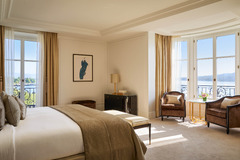 Spacious bedroom with king bed, French windows, and soft beige decor at The Woodward Geneva.