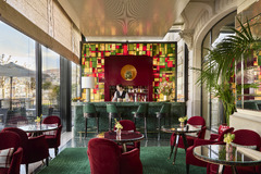 Vibrant cocktail bar at The Woodward Geneva with red velvet chairs, colorful glass accents, and lake views.