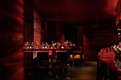 Dimly lit red and black interior of L’Atelier Robuchon Geneva, featuring counter seating and open kitchen.
