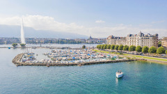 Panoramic view of Geneva’s waterfront with The Woodward hotel overlooking Lake Geneva and the Jet d’Eau fountain.